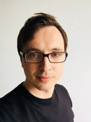 Chernikov mit Brille, kurzem dunklem Haar und schwarzem T-Shirt vor hellem Hintergrund.